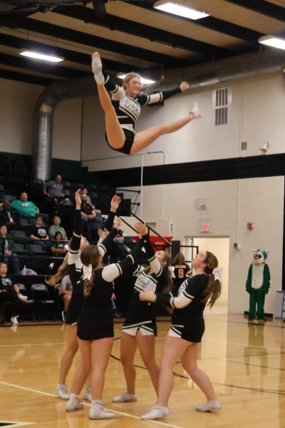 Cheerleaders throw junior Izabella Schierholz in a basket toss during the Homecoming assembly. The stut was part of their competitive routine.