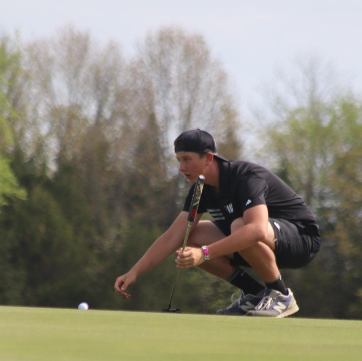 Freshman Jett Fluty kneels down to get a closer look before putting at the golf meet on April 15 against Adrian. 